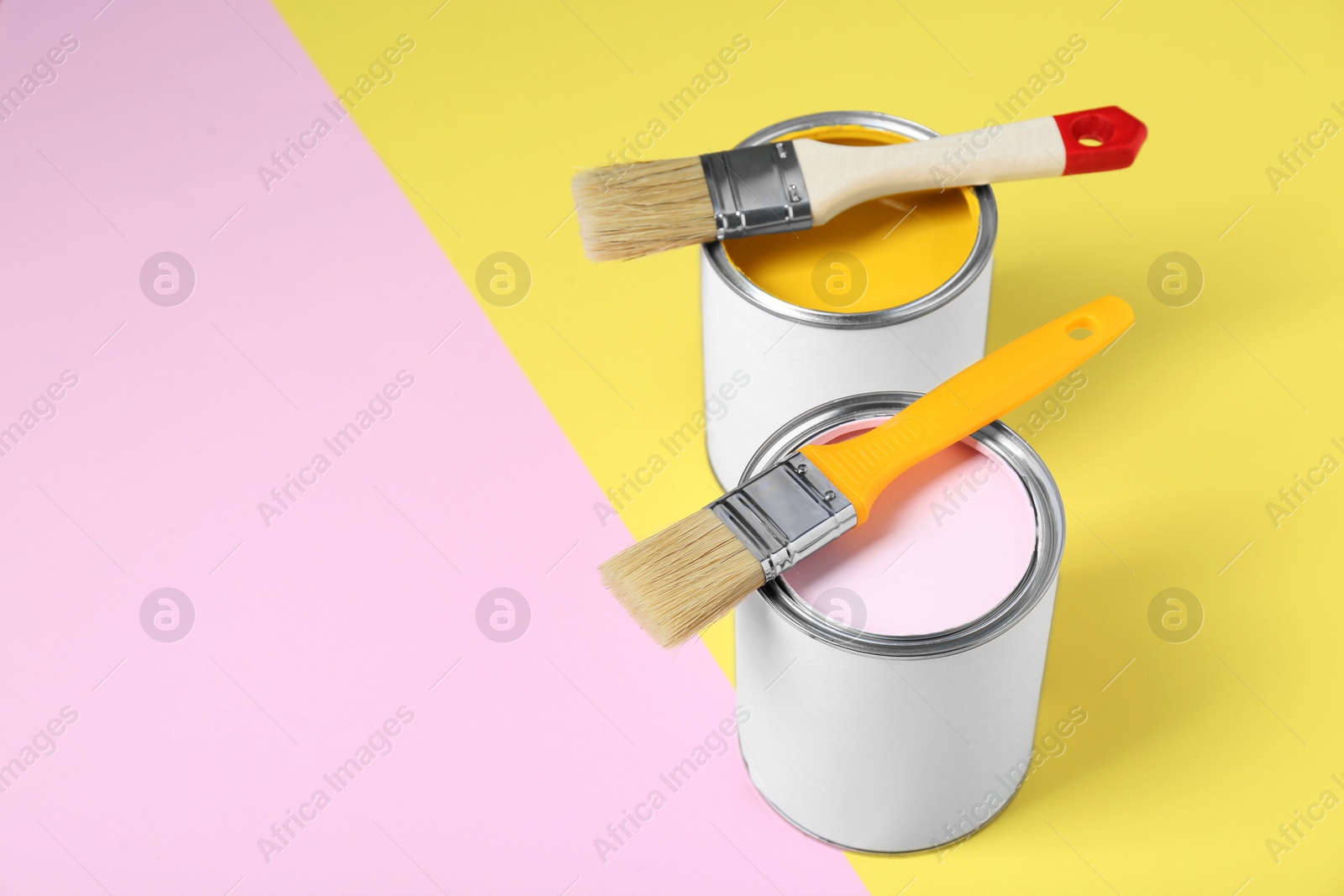 Photo of Cans of colorful paints with brushes on color background. Space for text