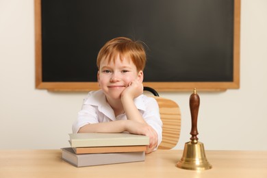 Photo of Cute little boy with books and school bell in classroom