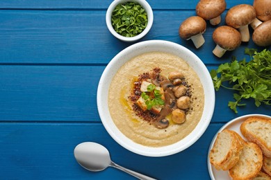 Photo of Delicious mushroom cream soup and ingredients on blue wooden table, flat lay. Space for text