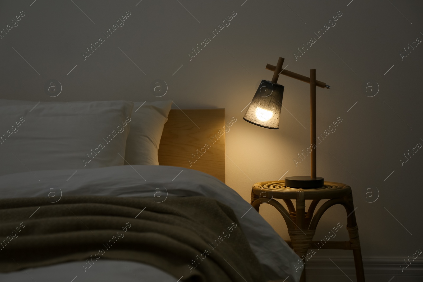 Photo of Stylish lamp on table near bed indoors