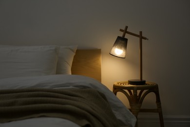 Photo of Stylish lamp on table near bed indoors