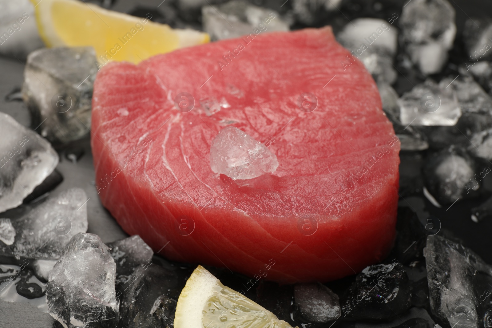 Photo of Raw tuna fillet and ice cubes on dark table, closeup