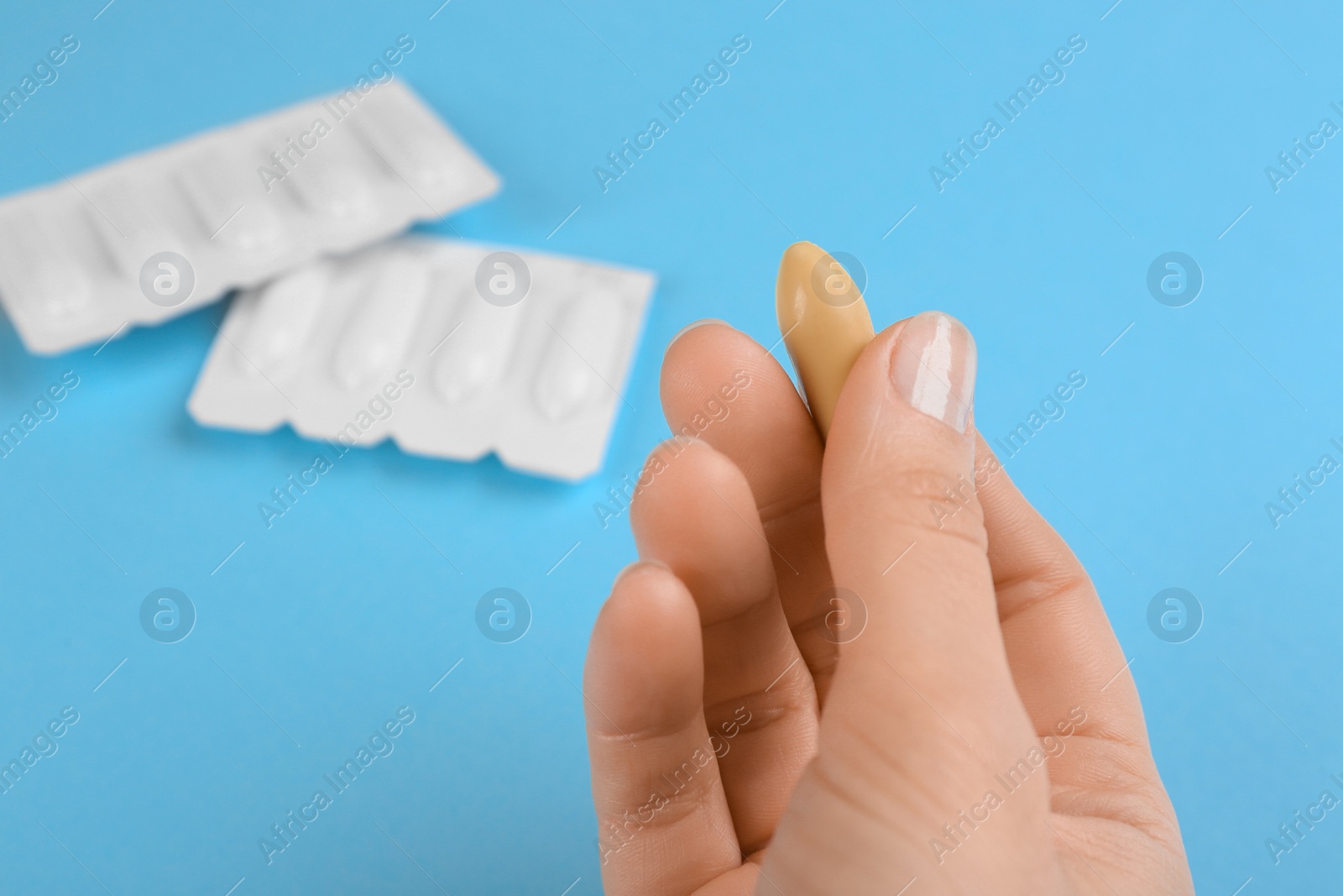 Photo of Woman holding suppository on light blue background, closeup. Hemorrhoid treatment