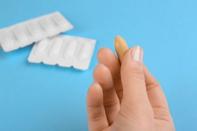 Photo of Woman holding suppository on light blue background, closeup. Hemorrhoid treatment