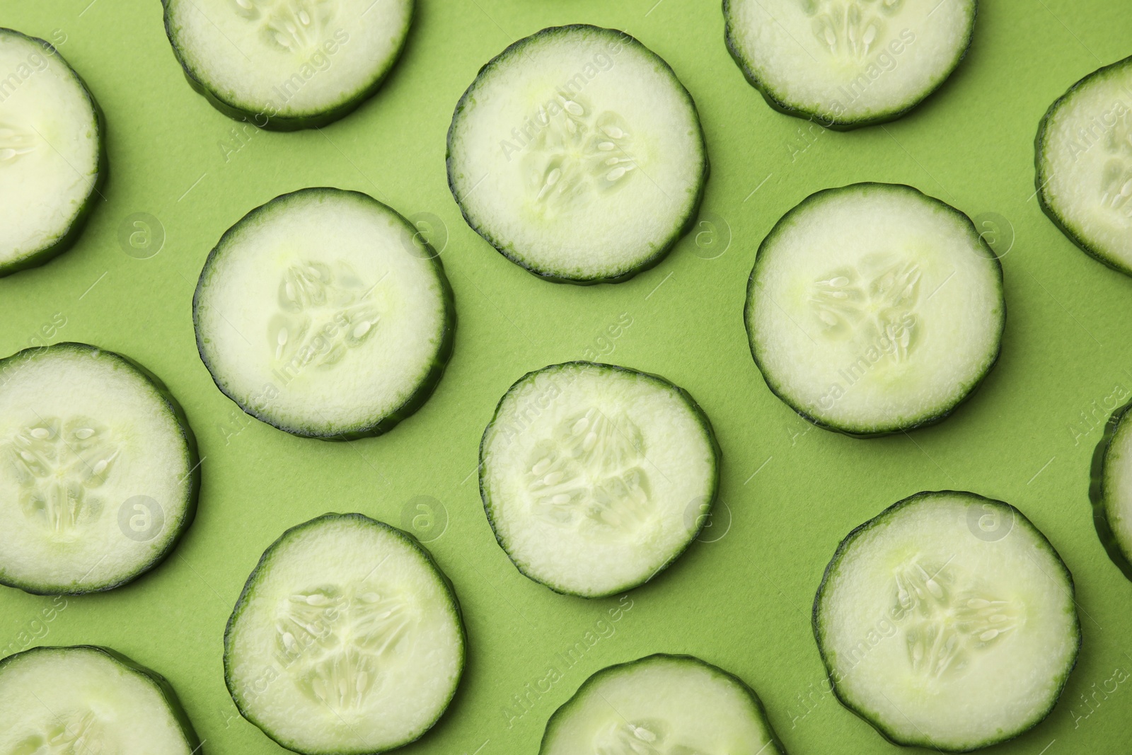 Photo of Fresh slices of cucumbers on green background, top view