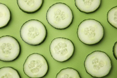 Fresh slices of cucumbers on green background, top view