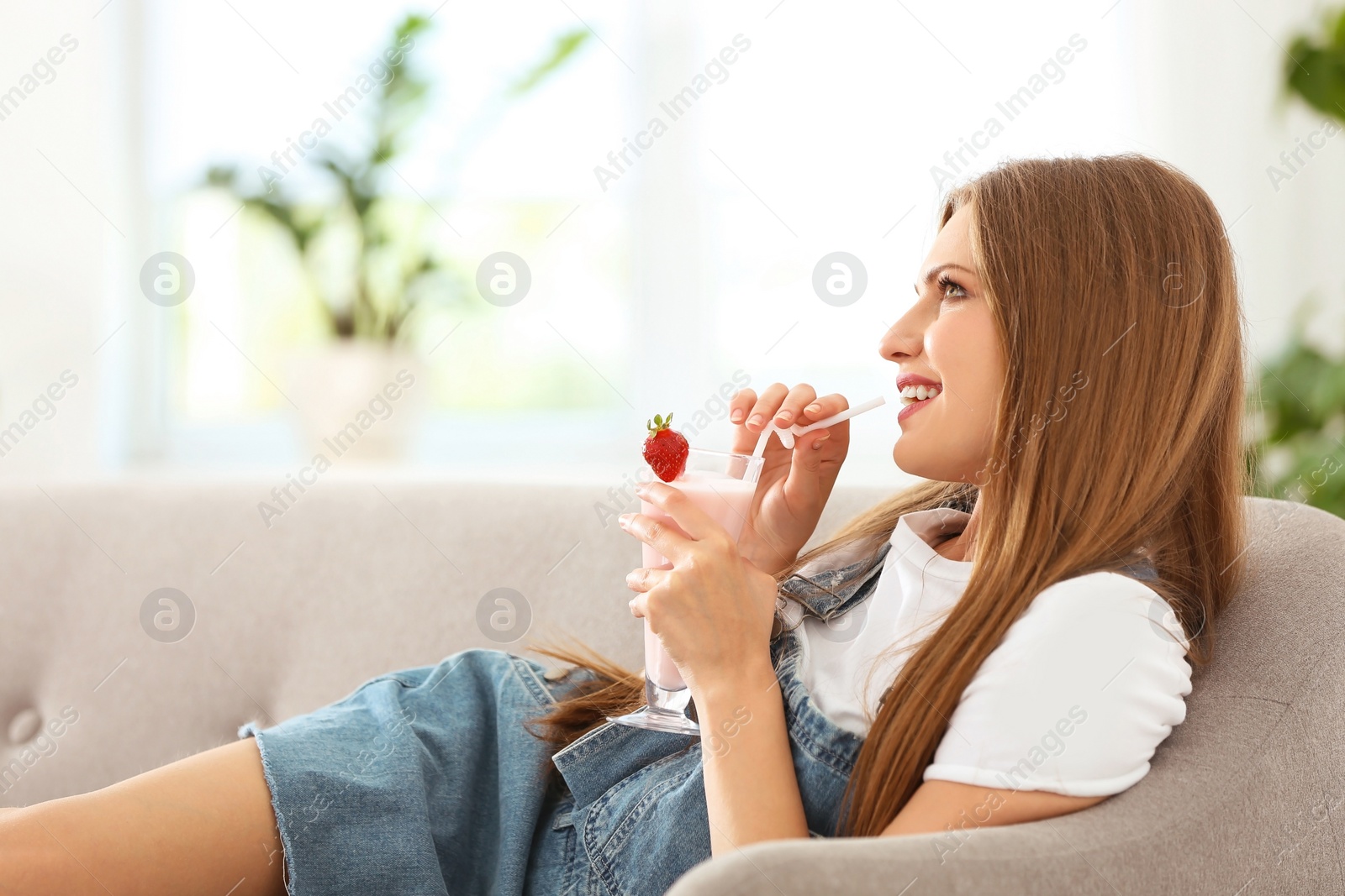 Photo of Young woman with glass of delicious milk shake indoors