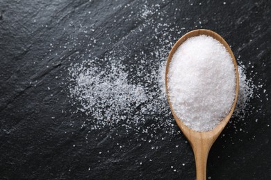 Organic white salt in spoon on black table, top view. Space for text