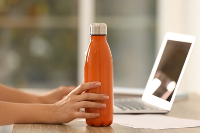 Photo of Woman with orange thermos bottle at workplace, closeup