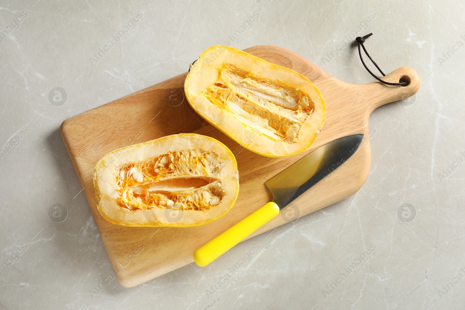 Photo of Wooden board with cut spaghetti squash and knife on gray background, top view