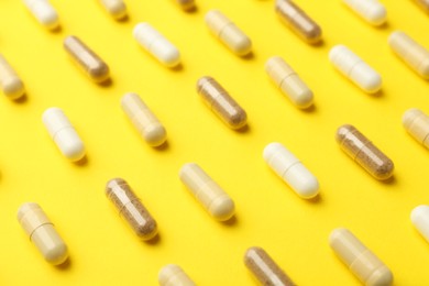 Photo of Different vitamin capsules on yellow background, closeup