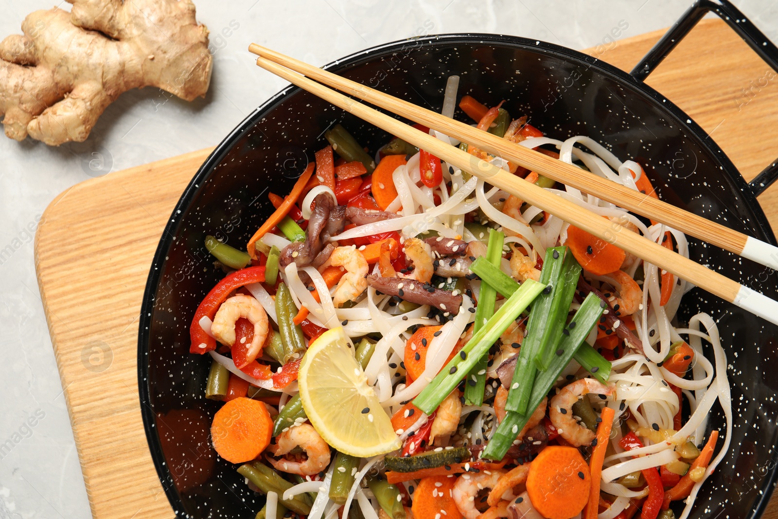 Photo of Shrimp stir fry with noodles and vegetables in wok on grey table, top view