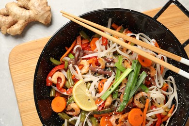 Shrimp stir fry with noodles and vegetables in wok on grey table, top view