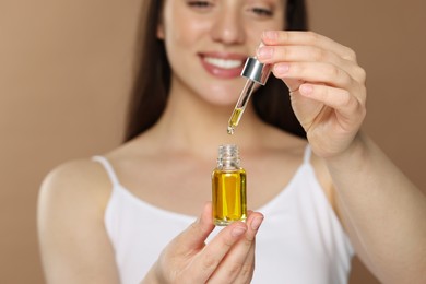 Photo of Woman with essential oil on brown background, selective focus