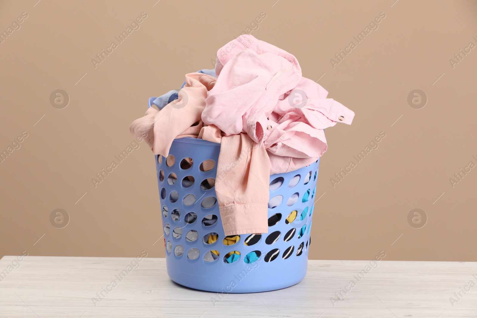 Photo of Plastic laundry basket with clothes near beige wall