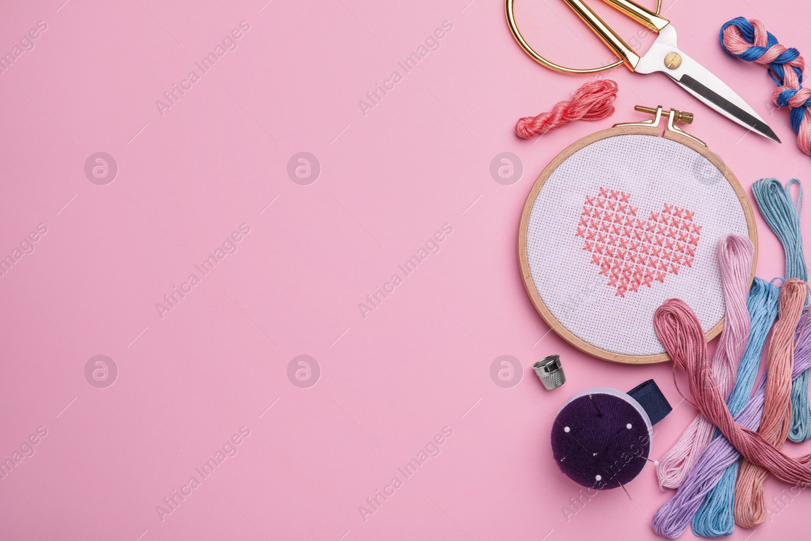 Photo of Flat lay composition with embroidery and different sewing accessories on pink background. Space for text