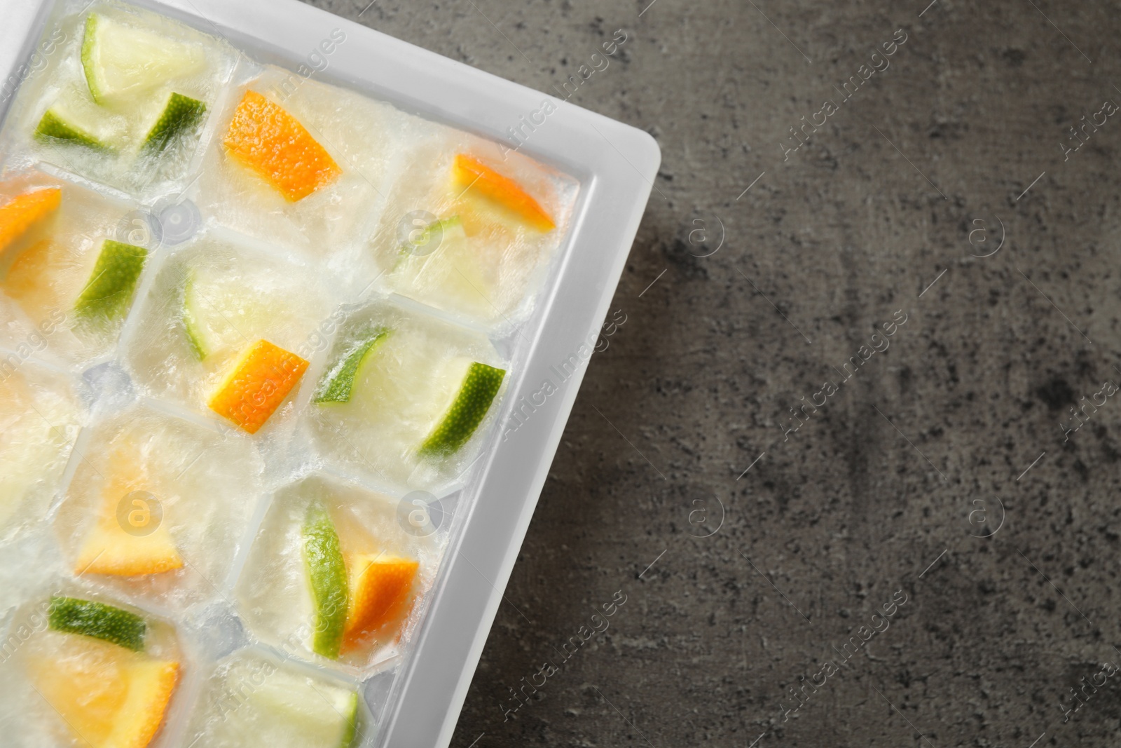 Photo of Ice cube tray with frozen fruits on grey table, flat lay. Space for text
