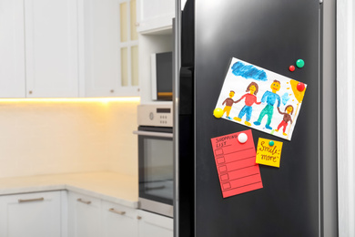 Photo of Modern refrigerator with child's drawing, notes and magnets in kitchen. Space for text