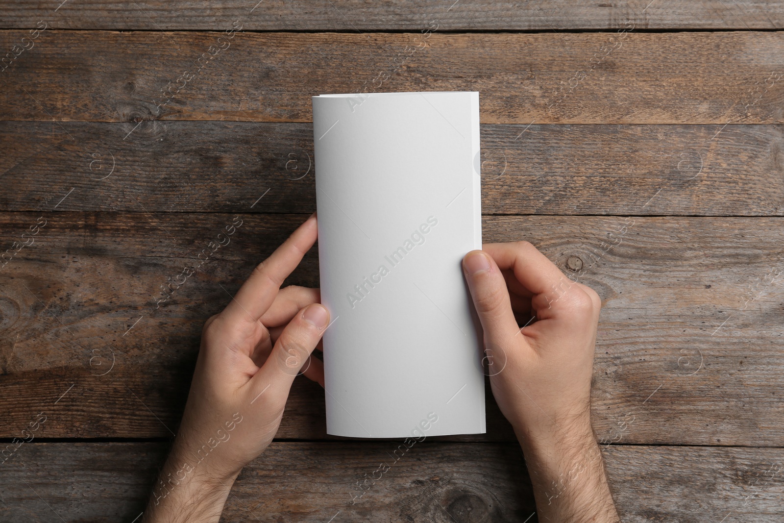 Photo of Man with blank brochure on wooden background, above view. Mock up for design