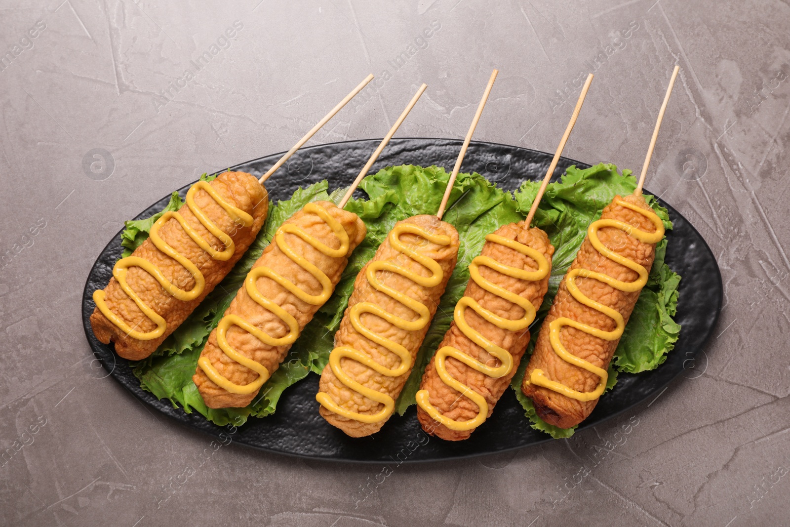 Photo of Delicious corn dogs with mustard on grey table, top view