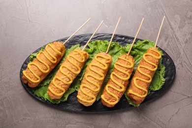 Delicious corn dogs with mustard on grey table, top view