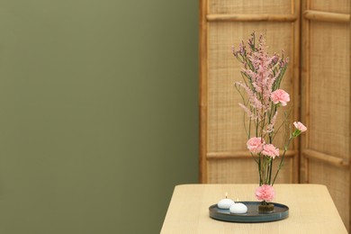 Photo of Stylish ikebana with beautiful pink flowers and burning scented candles carrying cozy atmosphere at home, space for text