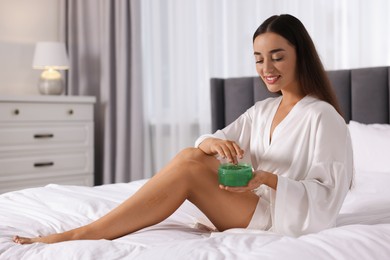 Photo of Young woman applying aloe gel onto her leg on bed indoors