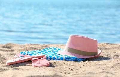 Photo of Bright towel, hat and flip flops on sand near sea. Beach object