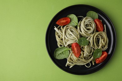 Tasty pasta with spinach, sauce and tomatoes on green table, top view. Space for text