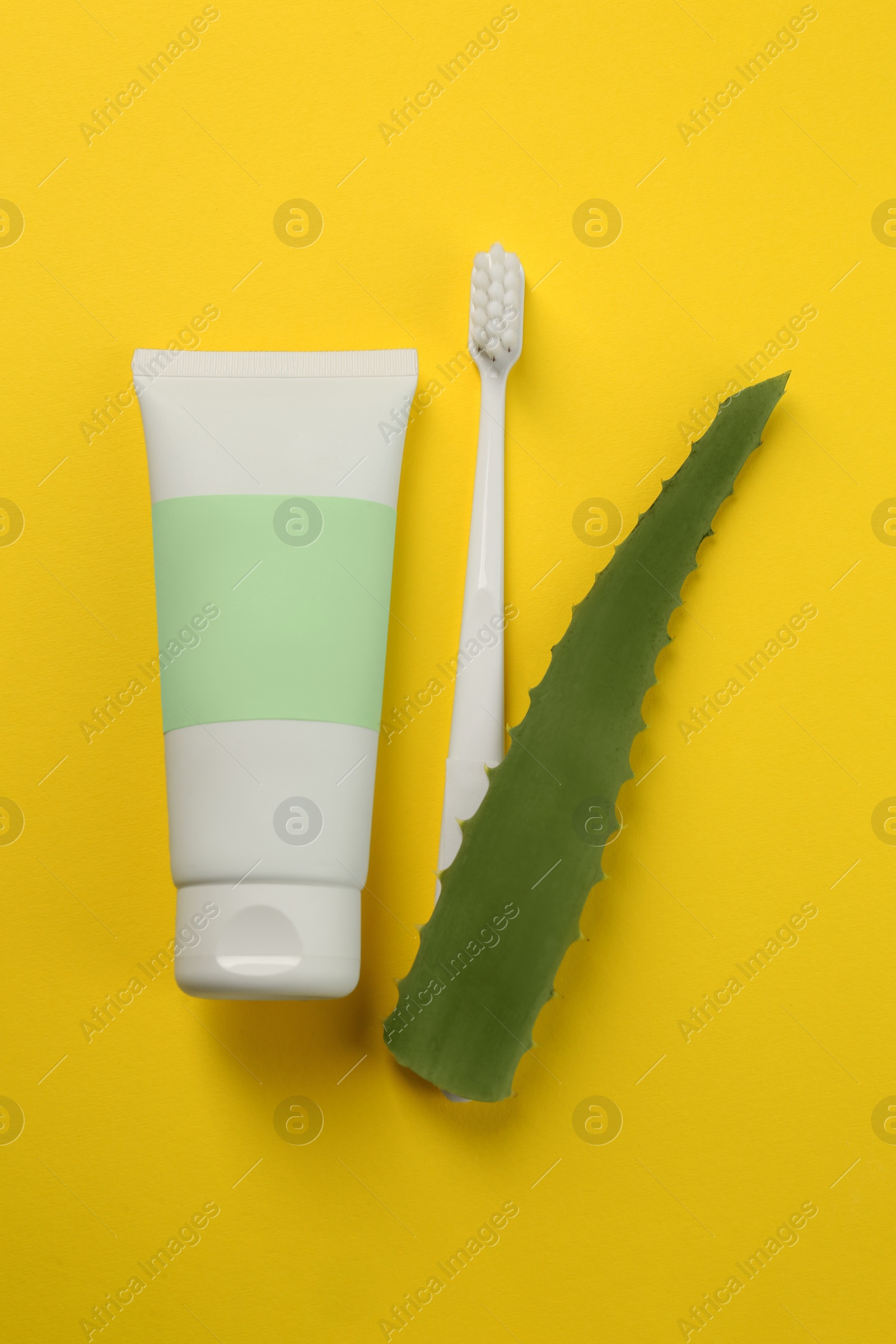 Photo of Aloe vera toothpaste in blank tube, brush and green leaf on yellow background, flat lay. Space for text