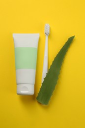 Aloe vera toothpaste in blank tube, brush and green leaf on yellow background, flat lay. Space for text