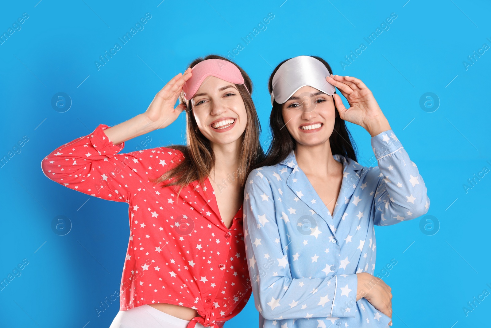 Photo of Beautiful women wearing sleeping masks on light blue background. Bedtime