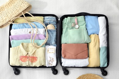 Photo of Open suitcase packed for trip and accessories on white blanket, flat lay