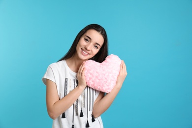 Photo of Portrait of young woman with decorative heart shaped pillow on color background