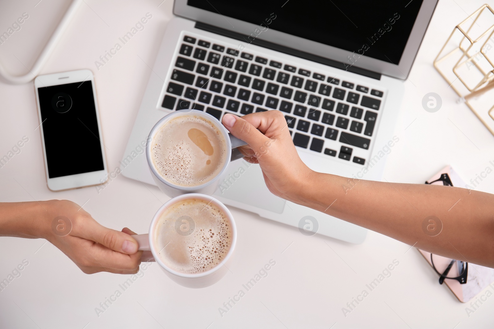 Photo of Women holding coffee cups at modern workplace in office, top view