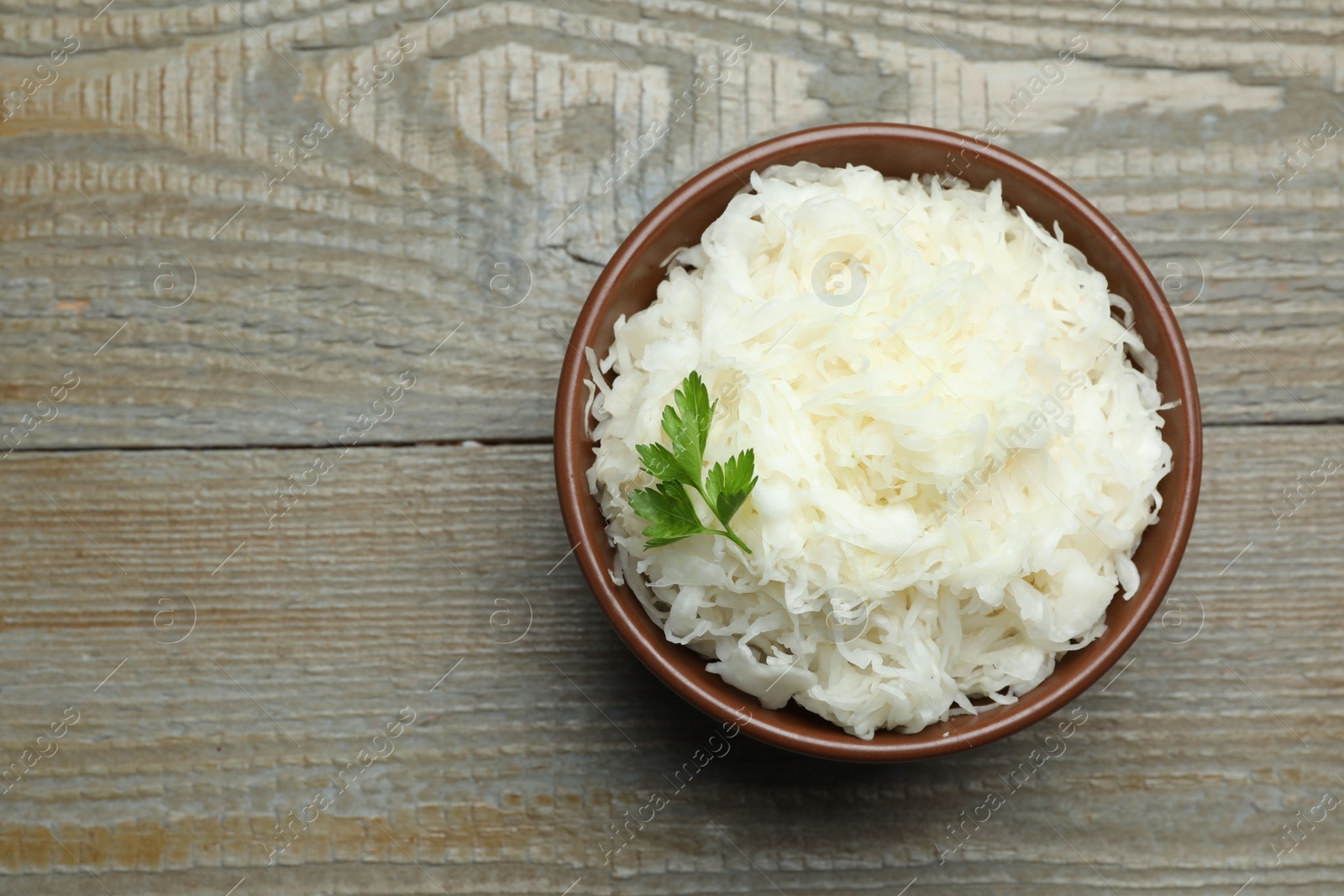 Photo of Tasty fermented cabbage with parsley on wooden table, top view. Space for text