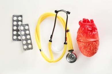 Photo of Stethoscope, pills and model of heart on light background. Heart attack concept
