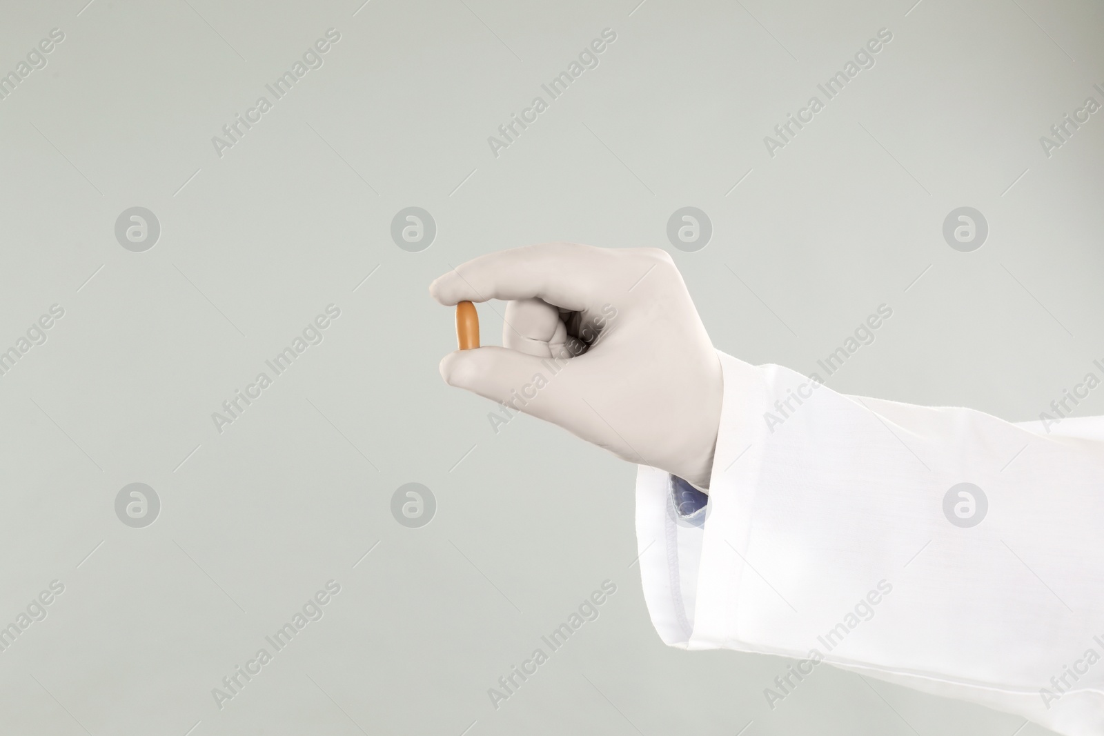 Photo of Doctor holding suppository for hemorrhoid treatment on light grey background, closeup