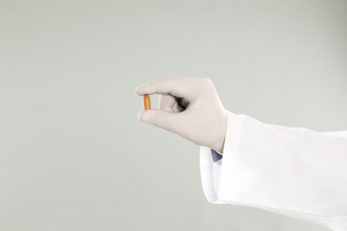 Doctor holding suppository for hemorrhoid treatment on light grey background, closeup
