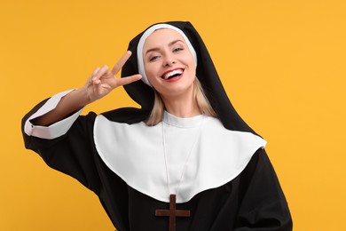 Photo of Happy woman in nun habit showing V-sign against orange background