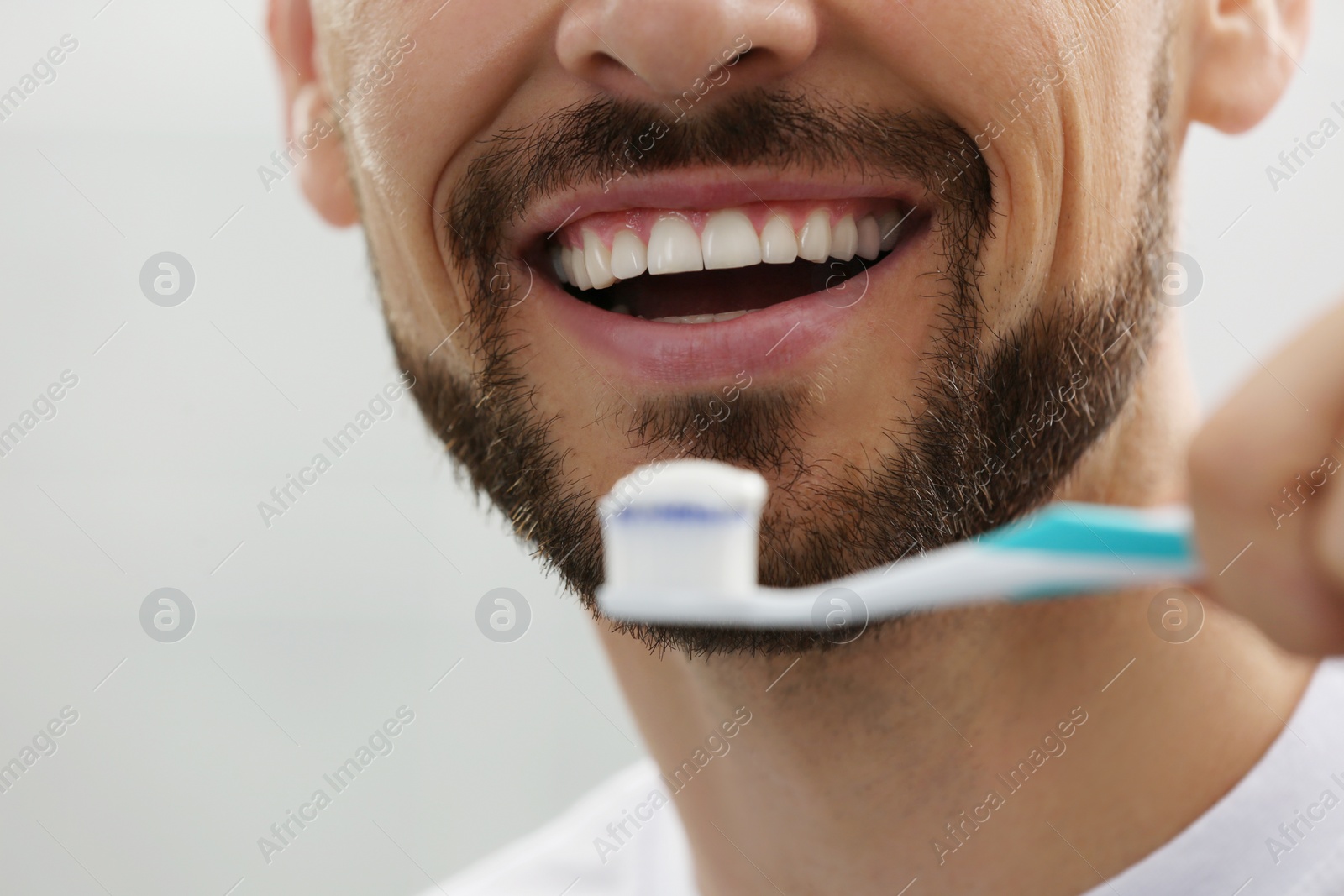 Photo of Man holding brush with toothpaste on grey background, closeup