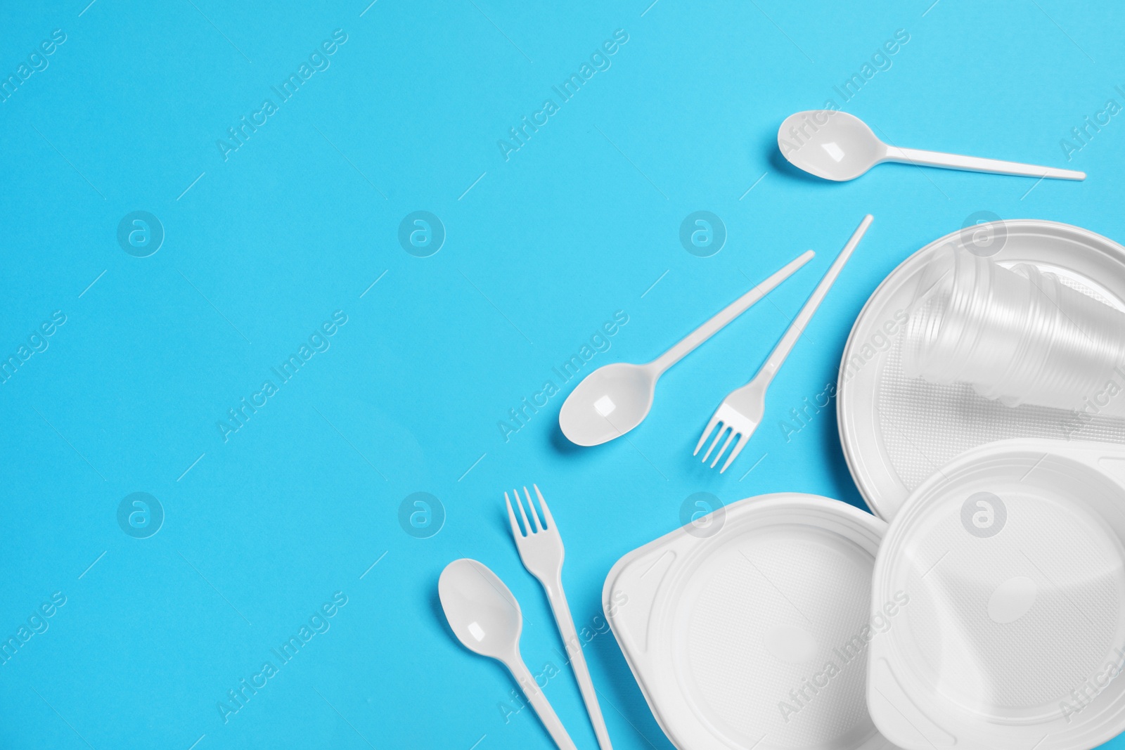 Photo of Disposable tableware on light blue background, flat lay. Space for text