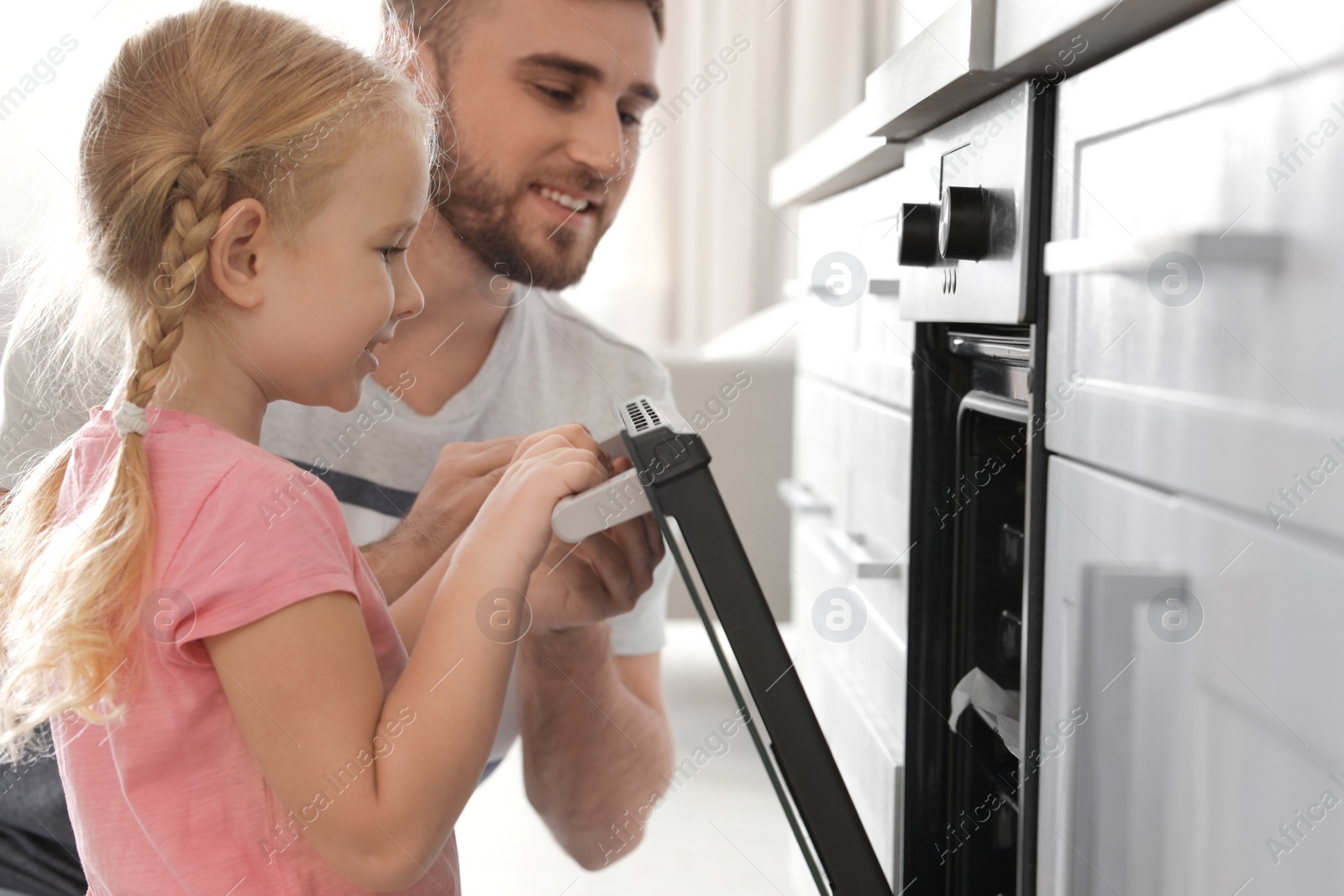 Photo of Father and daughter opening oven while baking in kitchen