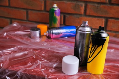 Photo of Used cans of spray paints on table near brick wall, space for text. Graffiti supplies