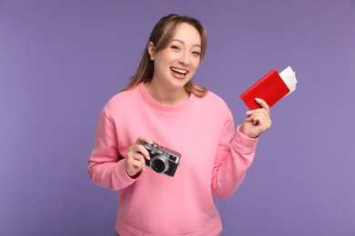 Happy young woman with passport, ticket and camera on purple background