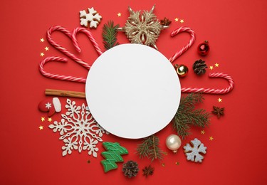 Flat lay composition with sweet candy canes, blank card and Christmas decor on red background, space for text