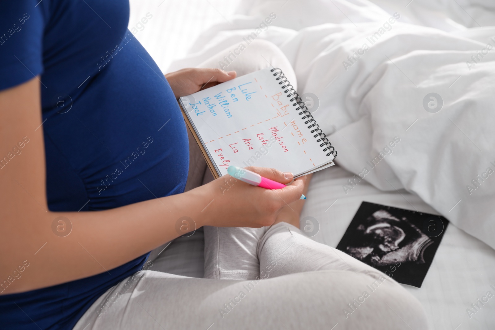 Photo of Pregnant woman with baby names list and sonogram sitting on bed, closeup