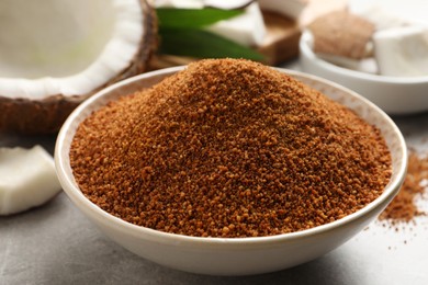 Natural coconut sugar in ceramic bowl on light grey table, closeup