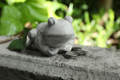 Photo of Frog figure with coins on stone parapet. Space for text