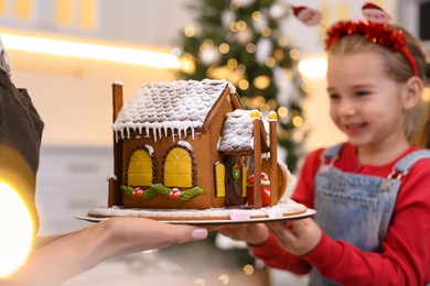 Photo of Mother and daughter with gingerbread house indoors, closeup